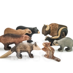 May include: A collection of wooden animal figurines, including a bear, bison, skunk, raccoon, and chipmunk. The figurines are hand-carved and painted in natural colors, showcasing the wood grain. These toys are designed for imaginative play.