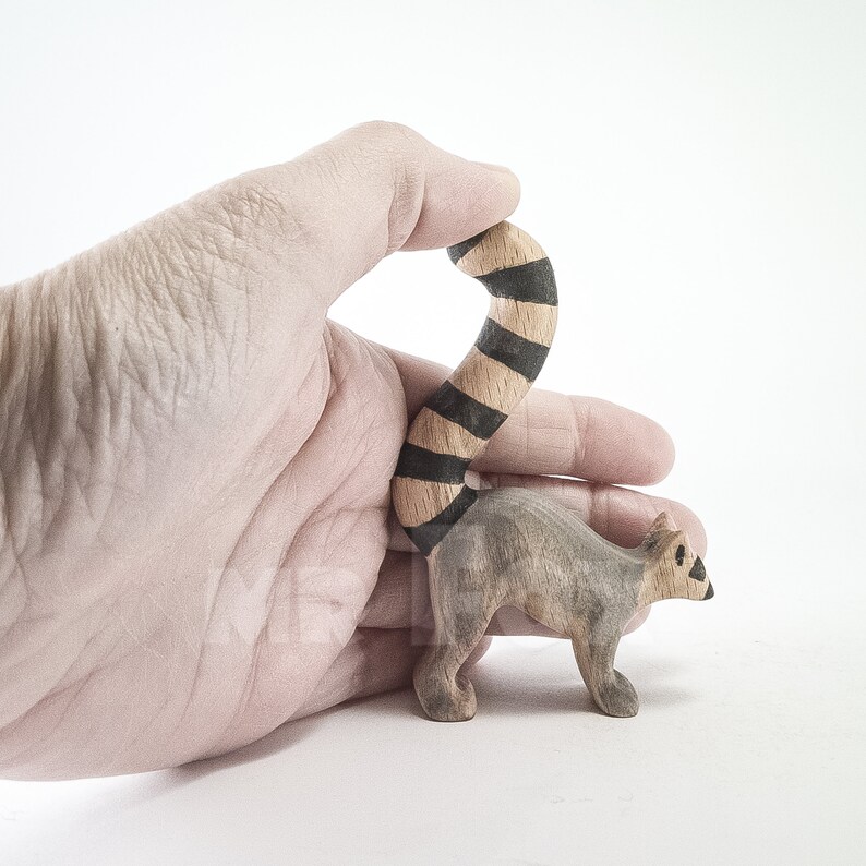 May include: A wooden hand-carved lemur figurine with a black and brown striped tail. The lemur is standing on a white surface.