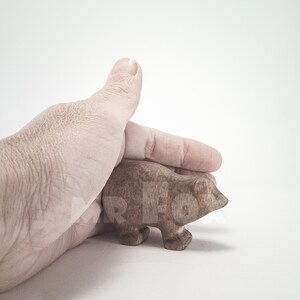 May include: A hand holding a small, wooden, brown bear figurine. The bear is standing on all fours and has a simple, carved design.