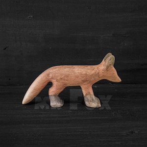 May include: A wooden fox figurine with a reddish-brown finish. The fox is standing on a black surface.