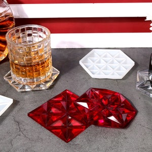 May include: Two red geometric coasters with a diamond pattern. The coasters are made of a clear material and have a shiny finish.