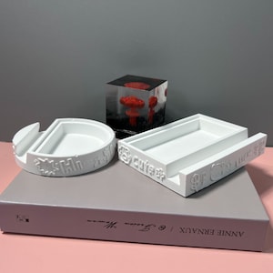 Puede incluir: Tres soportes de teléfono de resina blanca con detalles decorativos. Los soportes presentan las palabras "Hi-x-Star", "Cute" y "Oh-So-Cute".