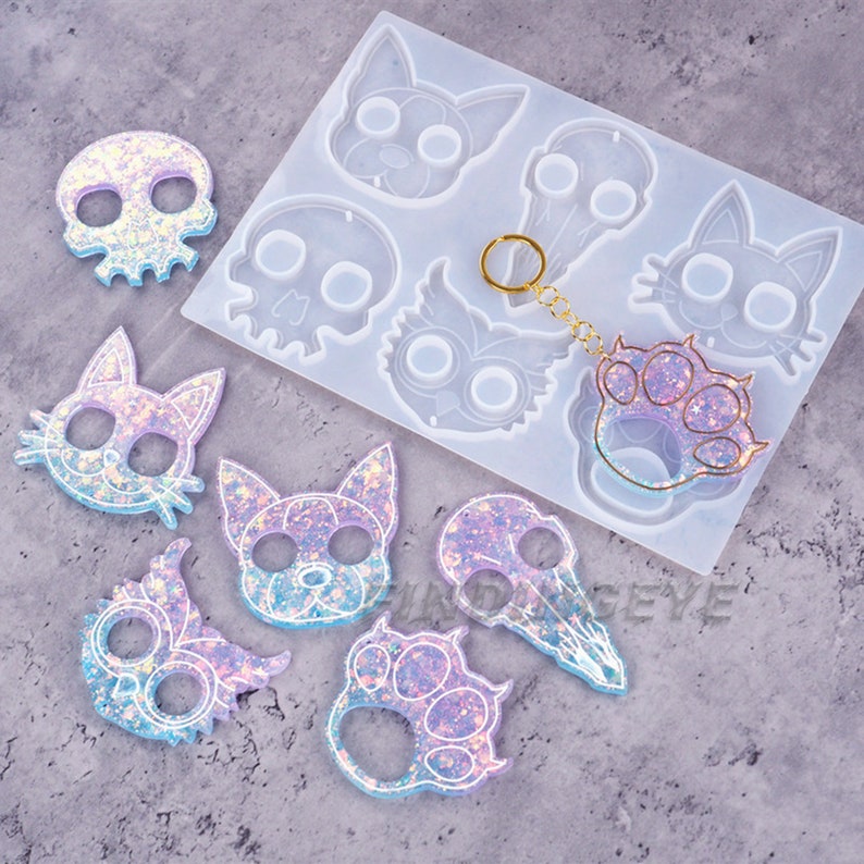 Pu&ograve; includere: Uno stampo in silicone con varie forme, tra cui un gatto, un teschio, un'impronta di zampa e un gufo. Ci sono anche diversi pezzi di resina finiti nelle forme dello stampo, con una finitura scintillante e iridescente.
