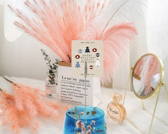May include: A blue resin photo holder with a floral design. The holder has a metal clip that holds a card with the text "Welcome 2021 Merry Christmas & Happy New Year Welcome 2021".