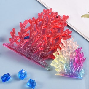 Puede incluir: Dos decoraciones de arrecife de coral en tonos rojos y arco&iacute;ris. Las decoraciones est&aacute;n hechas de un material transl&uacute;cido. Tambi&eacute;n hay tres piedras decorativas azules.