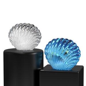 May include: Two decorative bottle stoppers shaped like seashells. The left stopper is clear and the right stopper is blue.