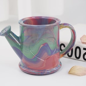 Może przedstawiać: Kolorowa ceramiczna konewka z wzorem serca. Konewka jest pomalowana w odcieniach różowego, niebieskiego, zielonego i fioletowego.