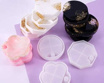 May include: Four silicone molds for making resin jewelry. The molds are in the shapes of a flower, a circle, a hexagon, and a square. Each mold has four compartments.