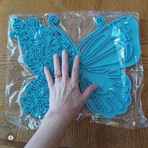 Op de afbeelding: Een grote, blauwe, vlinder-vormige wanddecoratie gemaakt van plastic. De vlinder heeft ingewikkelde details en een delicaat ontwerp.