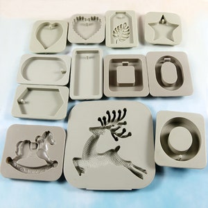 Puede incluir: Un conjunto de 12 moldes de silicona para manualidades de resina. Los moldes son de varias formas, incluyendo un corazón, una estrella, un reno, un caballo de balancín y una variedad de formas geométricas. Los moldes son todos grises y tienen un acabado liso y brillante.
