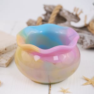 May include: A small, colorful glass bowl with a scalloped rim. The bowl is decorated with swirls of pink, blue, yellow, and green.