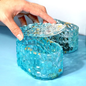 May include: A light blue resin trinket box with a honeycomb pattern and gold flecks. The box has a lid that is slightly open, revealing the interior.
