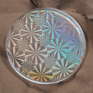 May include: A round, clear glass button with a repeating pattern of iridescent, starburst designs.