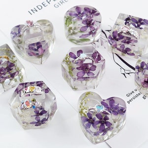 Può includere: Assortimento di porta anelli in resina trasparente con fiori secchi viola incorporati. Ogni porta anelli ha una forma diversa, tra cui un cuore, un esagono e un cerchio. I porta anelli sono perfetti per esporre anelli e altri piccoli gioielli.