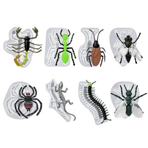May include: A collection of insect-themed molds, including a scorpion, ant, cockroach, fly, spider, lizard, centipede, and another fly. Each insect is a different color, with details like wings and segmented bodies. The molds are set against a white background.