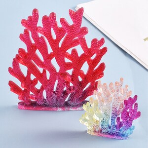 Puede incluir: Dos esculturas decorativas de arrecifes de coral. La m&aacute;s grande es de un rojo vibrante, mientras que la m&aacute;s peque&ntilde;a muestra un degradado de colores, incluyendo amarillo, rosa y morado. Ambas tienen estructuras ramificadas intrincadas.