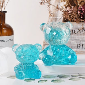 May include: Two blue resin teddy bear figurines. The larger bear is sitting with its legs crossed and the smaller bear is sitting with its legs straight out in front of it.