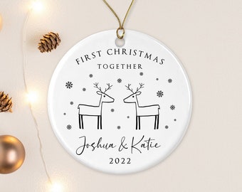 Pode incluir: Adorno de Natal de cerâmica branca com um contorno preto de duas renas que se olham. O adorno diz "First Christmas Together" com os nomes "Joshua & Katie" e o ano "2022" abaixo das renas.