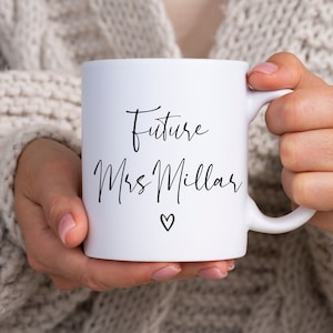May include: White ceramic mug with black text that reads "Future Mrs. Millar" and a small heart.