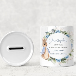 May include: White ceramic money box with a blue and green floral design featuring a rabbit and the text "Christopher on your christening day 23.02.2022 All Saints Church".