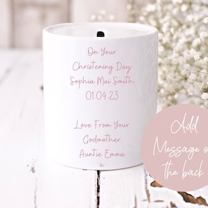 May include: White ceramic money box with a pink inscription that reads "On Your Christening Day Sophia Mai Smith 01.04.23 Love From Your Godmother Auntie Emma". A pink circle with the text "Add Message on the back" is in the lower right corner.