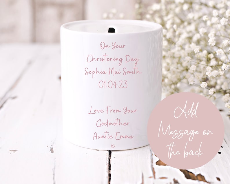 May include: White ceramic money box with a pink inscription that reads "On Your Christening Day Sophia Mai Smith 01.04.23 Love From Your Godmother Auntie Emma". A pink circle with the text "Add Message on the back" is in the lower right corner.