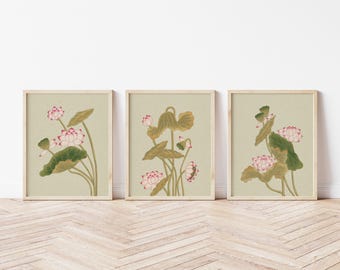 May include: Three framed botanical prints featuring lotus flowers. Each print showcases a different arrangement of pink and white lotus blossoms, green leaves, and stems against a muted green background. The frames are light-colored wood.