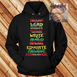 Peut inclure: Sweat-shirt noir avec un motif rouge, jaune et vert. Le texte sur le sweat-shirt est "Dream Like Martin, Lead Like Harriet, Fight Like Malcolm, Think Like Garvey, Write Like Maya, One Like Madam CJ, Speak Like Frederick, Educate Like WEB, Believe Like Thurgood, Challenge Like Rosa."