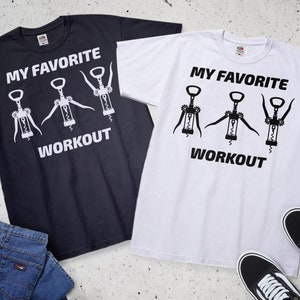 May include: Two t-shirts with a graphic of three corkscrews and the text "My Favorite Workout". One t-shirt is black with white text and graphics, and the other is white with black text and graphics.