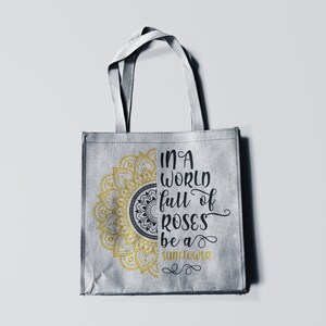 May include: A gray tote bag with a gold mandala design and the text "In a world full of roses be a sunflower" printed on it.