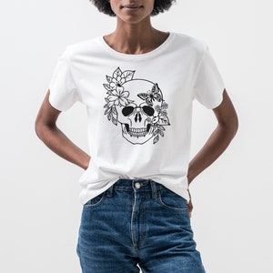 K&ouml;nnte beinhalten: Ein wei&szlig;es T-Shirt mit einem schwarz-wei&szlig;en Motiv eines Sch&auml;dels, der mit Blumen und einem Schmetterling verziert ist.