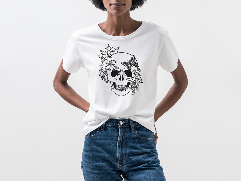 K&ouml;nnte beinhalten: Ein wei&szlig;es T-Shirt mit einem schwarz-wei&szlig;en Motiv eines Sch&auml;dels, der mit Blumen und einem Schmetterling verziert ist.