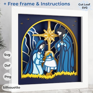 Può includere: Una cornice bianca con un design intagliato in carta blu e oro che rappresenta la scena della Natività. La scena include Maria, Giuseppe e il bambino Gesù. Il design è a più strati e ha un effetto 3D. La cornice è etichettata "Cut Leaf SVG".