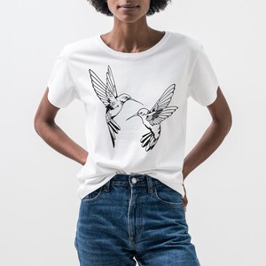 May include: White t-shirt with a black graphic of two hummingbirds in flight.