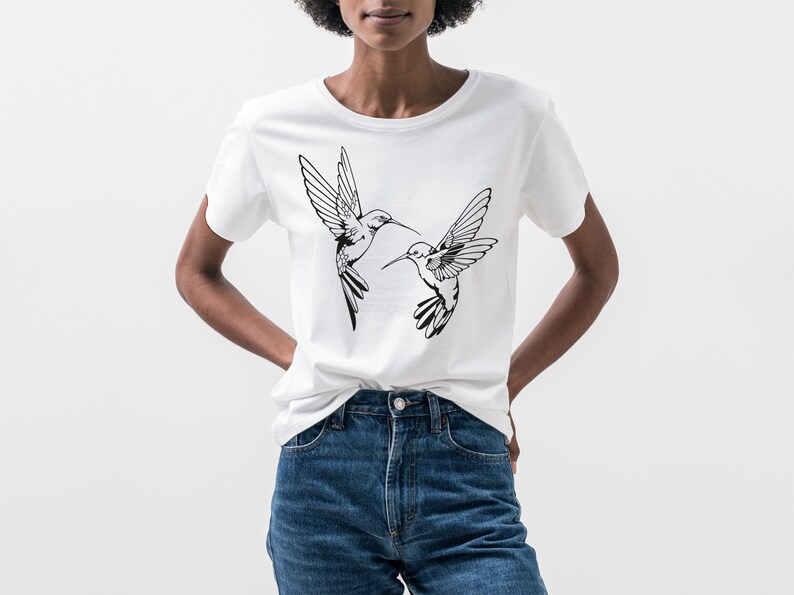 May include: White t-shirt with a black graphic of two hummingbirds in flight.