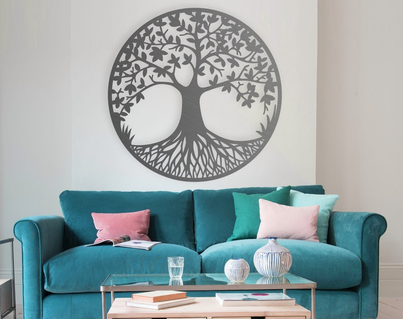 May include: A teal blue sofa with three pillows, two pink and one green, sits in front of a white wall with a large gray metal tree of life wall decor.