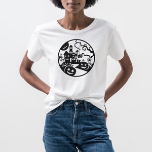May include: White t-shirt featuring a black Halloween-themed graphic. The design includes a haunted house, pumpkins, bats, and a spider, all within a circular frame. The shirt is made of a soft material and is suitable for casual wear.