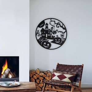 May include: Black metal Halloween wall art featuring a haunted house, pumpkins, a bat, and a spider within a circular frame. The artwork is displayed on a white wall above a wooden table and a leather chair.