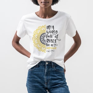 May include: White t-shirt with a yellow and black mandala design and the text "In a world full of roses be a sunflower".