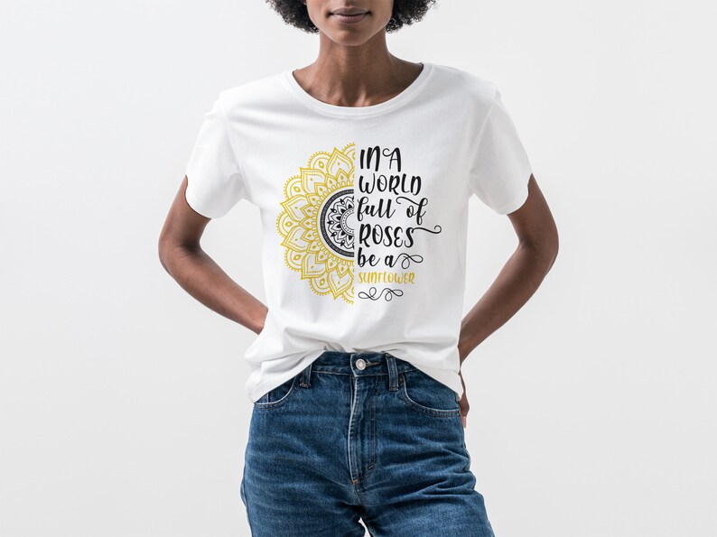 May include: White t-shirt with a yellow and black mandala design and the text "In a world full of roses be a sunflower".