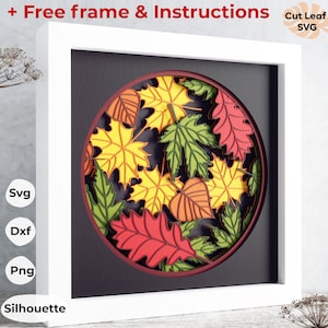 May include: A white frame with a black mat surrounding a round, layered paper art piece. The art features a variety of fall leaves in shades of red, orange, yellow, and green. The text "Cut Leaf SVG" is in the upper right corner of the image.