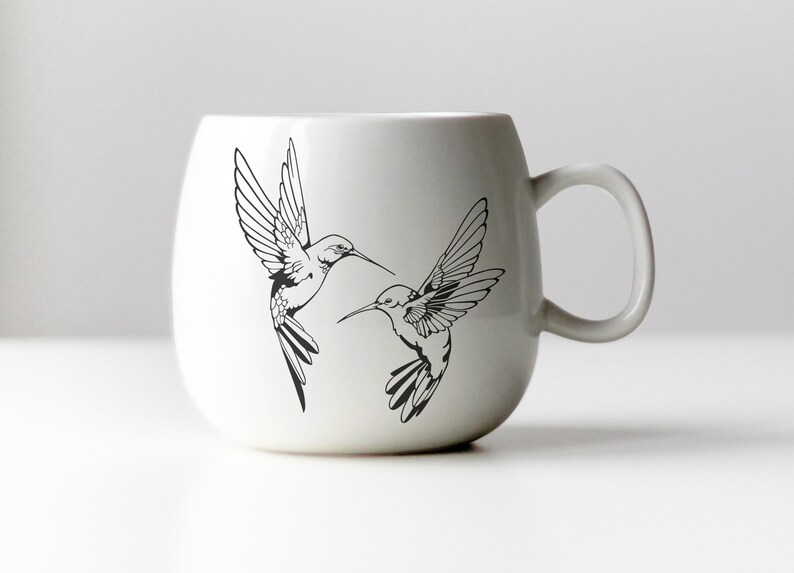 May include: White ceramic mug with a black line drawing of two hummingbirds in flight.
