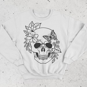 K&ouml;nnte beinhalten: Wei&szlig;er Pullover mit einem schwarz-wei&szlig;en Motiv eines Sch&auml;dels, der mit Blumen und einem Schmetterling verziert ist.