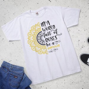 May include: White t-shirt with a yellow and black mandala design and the text "In a world full of roses be a sunflower".