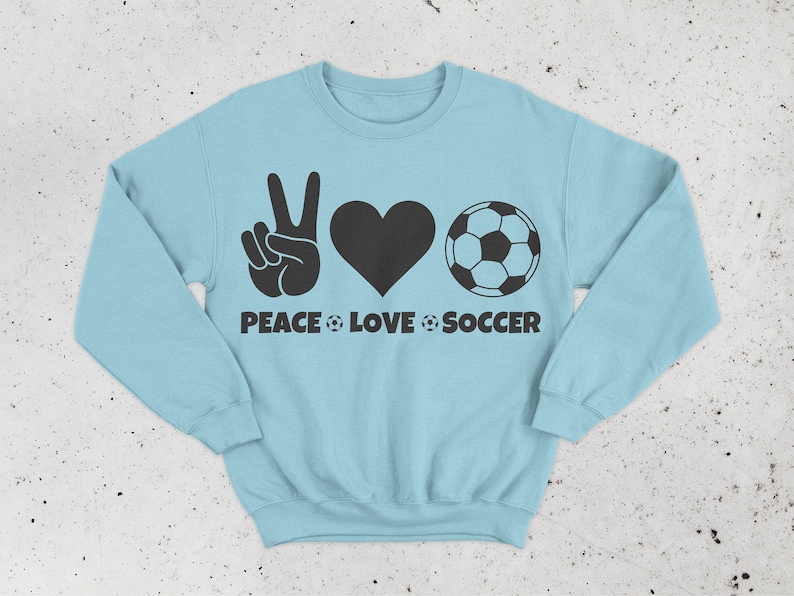 May include: Light blue sweatshirt with a black graphic design. The design includes a peace sign, a heart, and a soccer ball, with the words "PEACE LOVE SOCCER" below. The sweatshirt is a crew neck style.