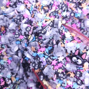 Puede incluir: Primer plano de una variedad de amuletos de resina de colores, incluyendo estrellas y personajes de dibujos animados. Los amuletos son de varios colores, incluyendo rosa, azul, amarillo y verde.