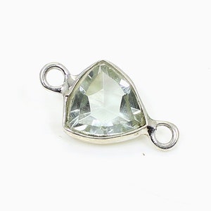 Può includere: Un ciondolo triangolare di pietra preziosa verde pallido con montatura in metallo color argento. Il ciondolo ha una superficie sfaccettata e piccoli anelli su ogni lato per il fissaggio a una catena o ad altro componente di gioielleria. La pietra preziosa è larga circa 2 cm.