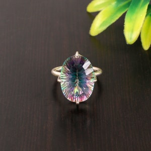 Puede incluir: Un anillo de plata con una gran piedra preciosa ovalada iridiscente. La piedra preciosa presenta un arcoíris de colores, incluyendo azul, verde, morado y rosa.