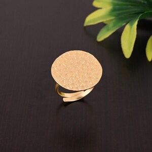 Pode incluir: Um anel dourado com uma parte superior redonda e texturizada. A parte superior do anel tem um design martelado e texturizado.