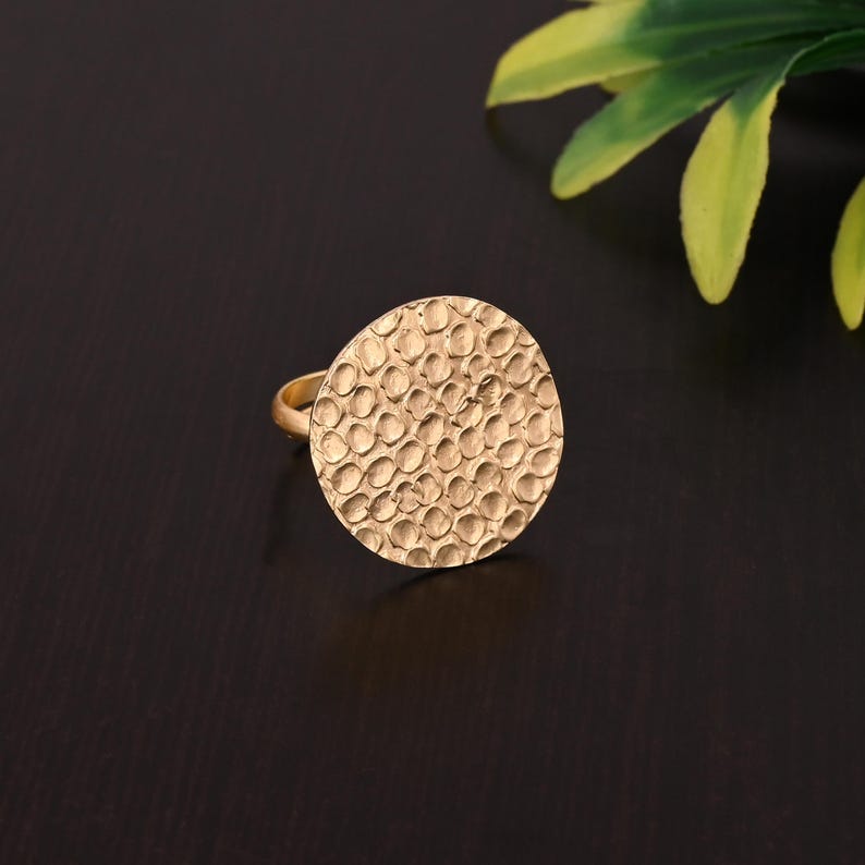 Pode incluir: Um anel dourado com um design circular texturizado. O anel &eacute; feito de metal e tem um acabamento martelado.